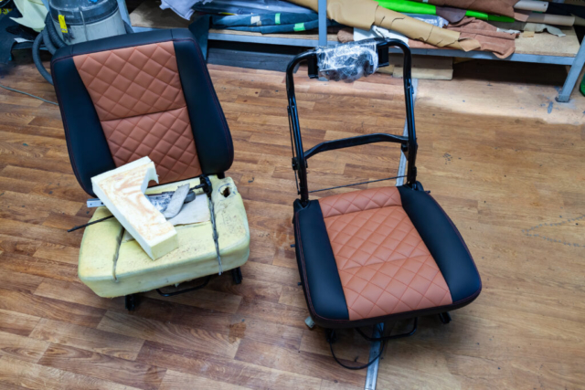 Two front seats with combined leather trim in double colors of black and brown with shape of rhombus and the visible part of the frame located on the floor in the workshop for repair and tuning of car